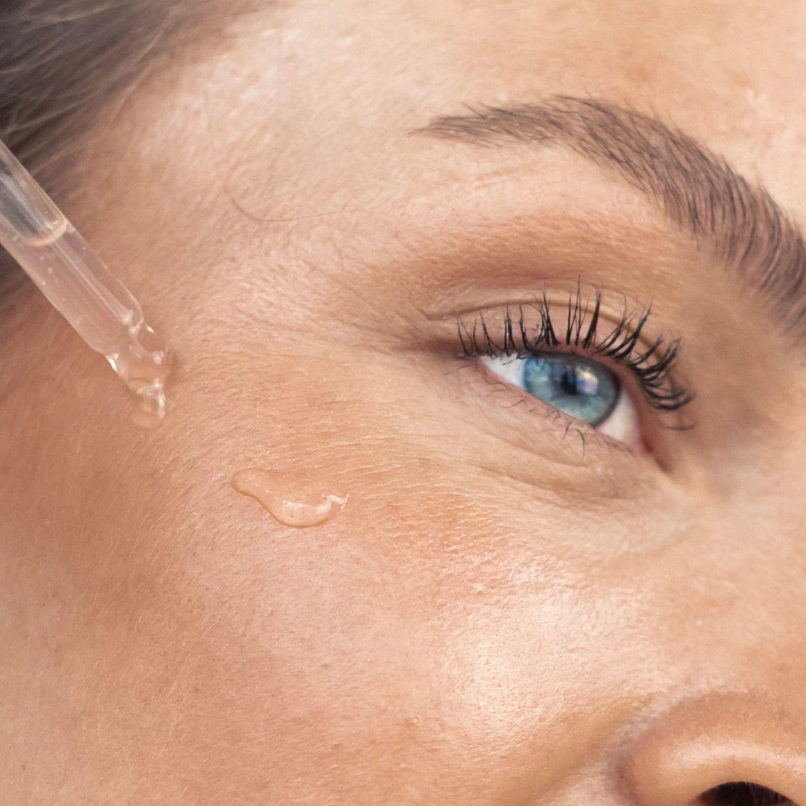 A close-up of a woman applying Glow Serum to her skin, emphasizing its luminous and hydrating effects.