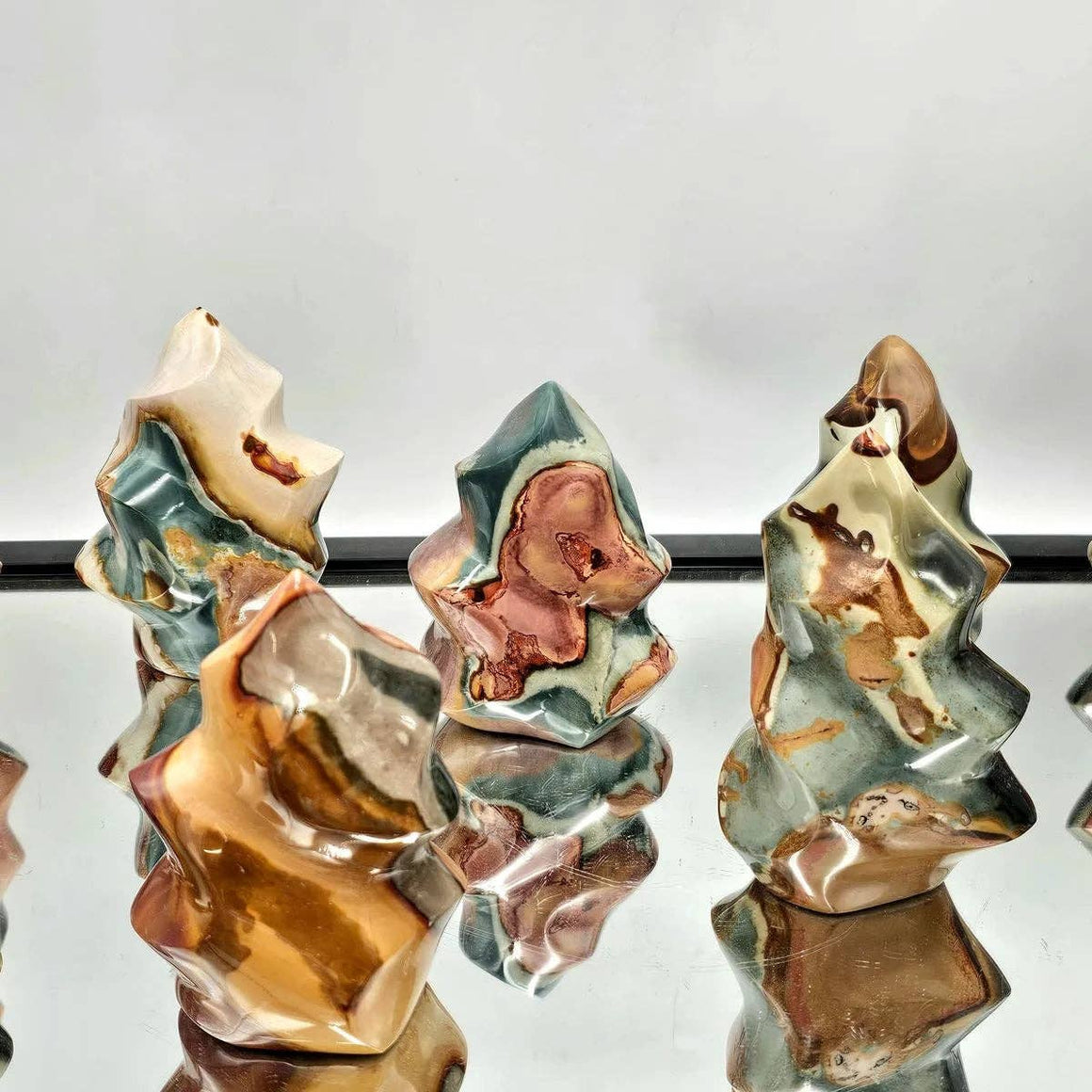 Three ceramic sculptures with earthy tones on a reflective surface