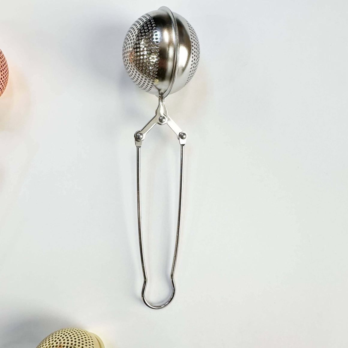Metallic tea ball infuser on a light gray background
