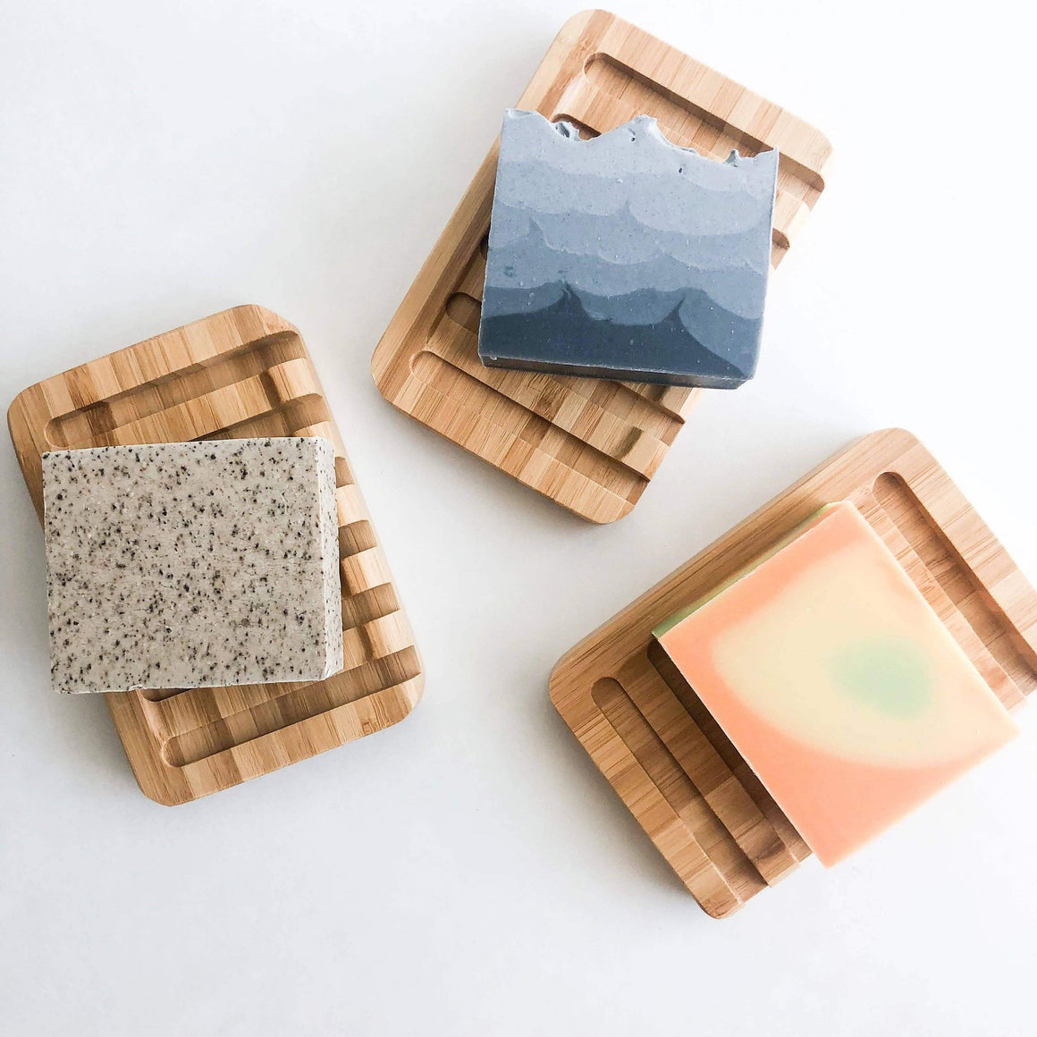 Three wooden soap dishes with different soaps on a white background