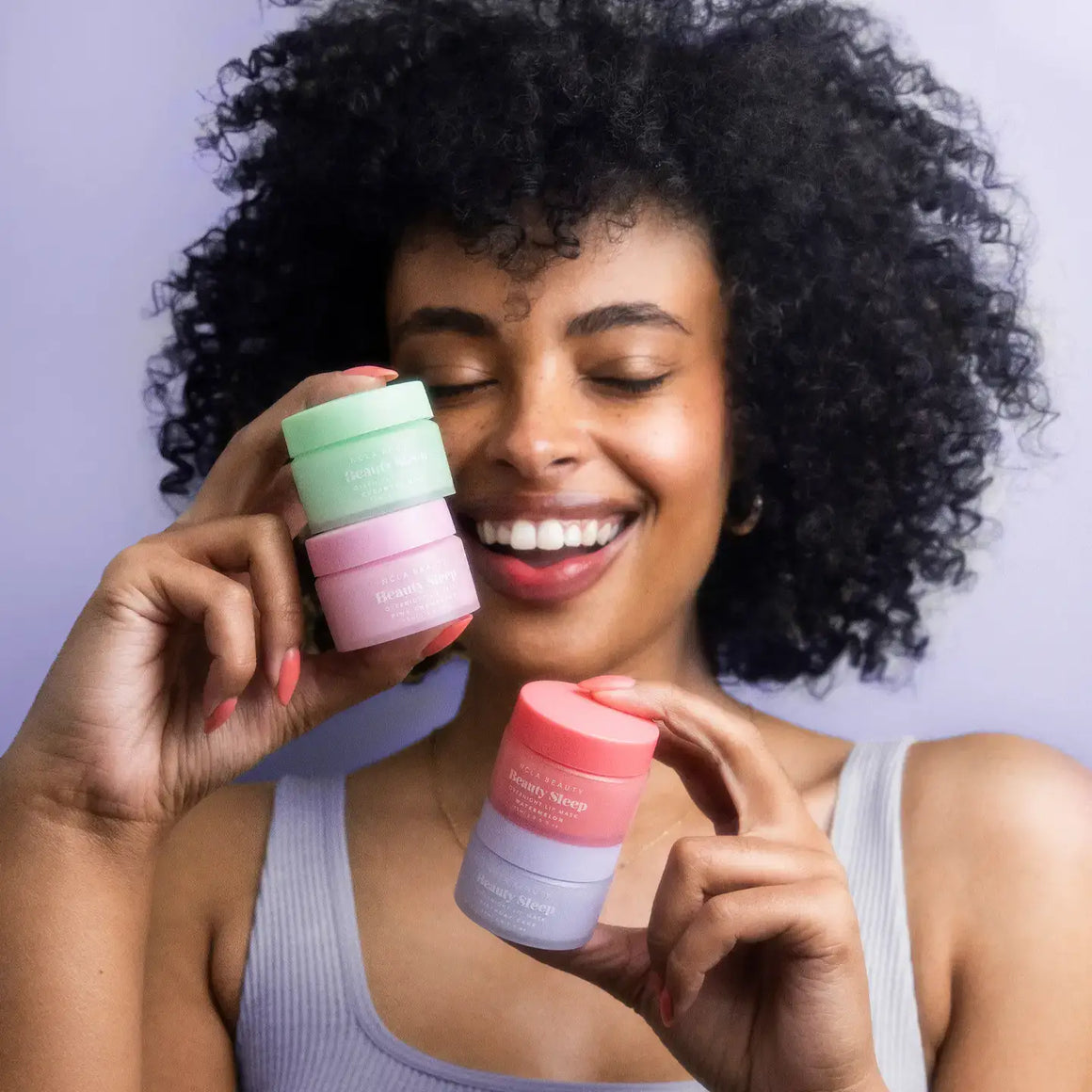Happy woman holding three colorful jars of overnight lip masks with healthy, hydrated skin and curly hair.