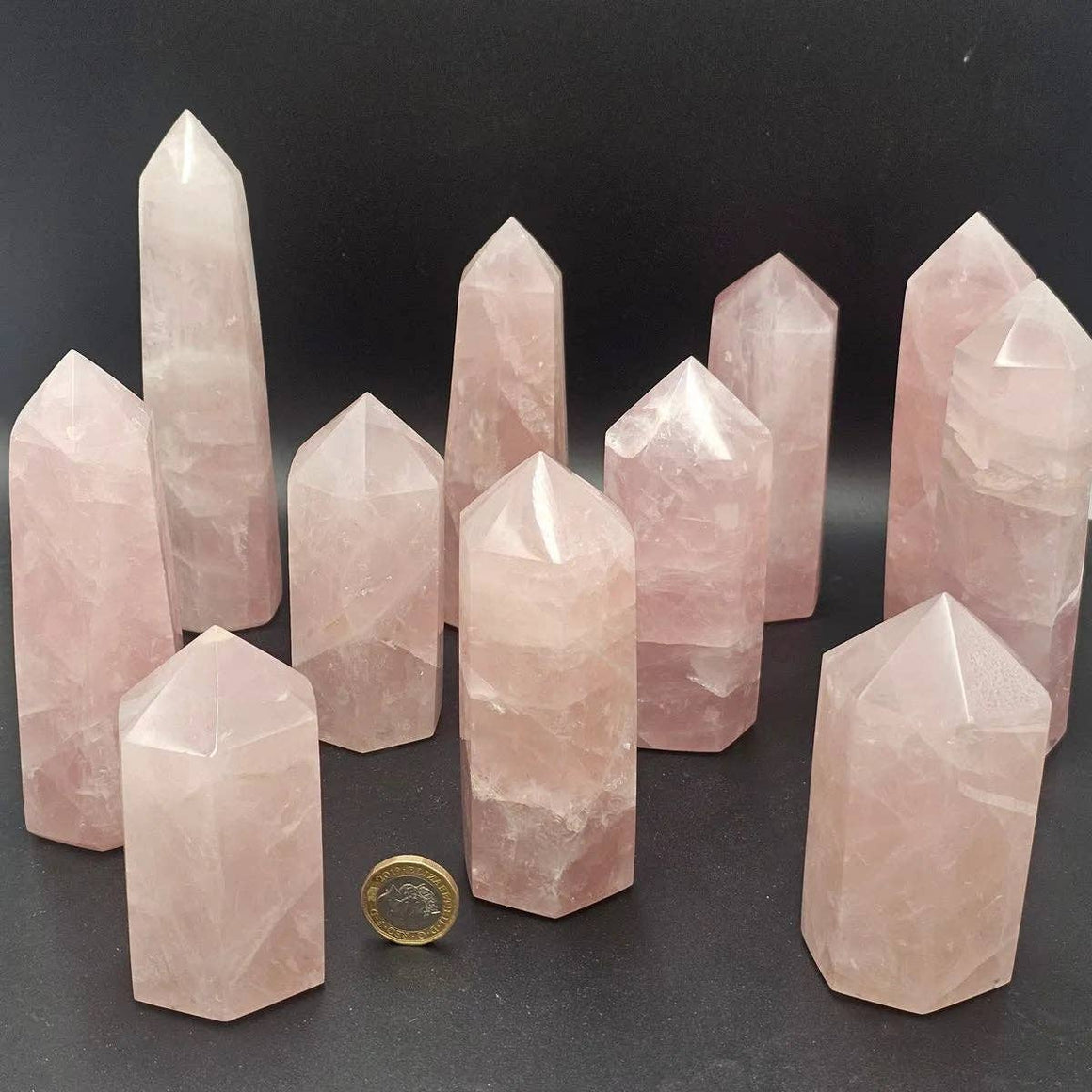 Collection of rose quartz crystal points on a dark surface with a coin for scale.