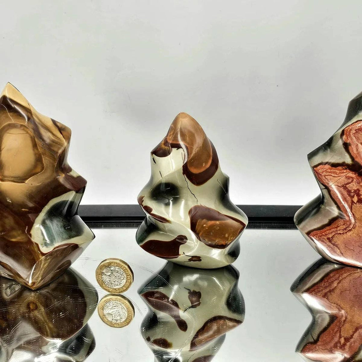 Close-up of three brown and silver beads on a reflective surface with a coin for scale.