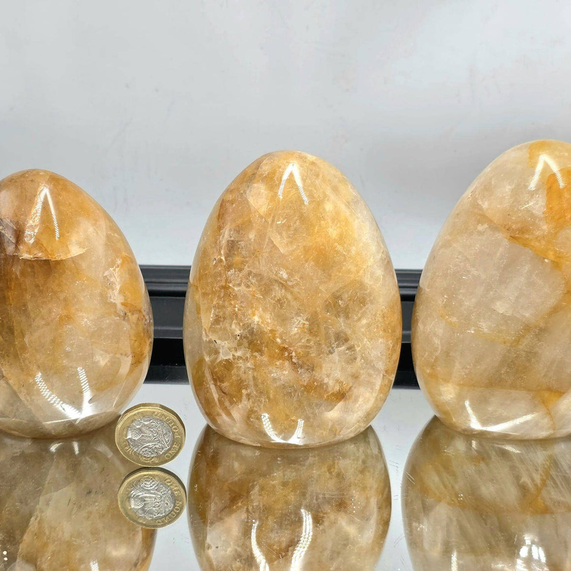 Three large orange stones on a reflective surface with a light gray background