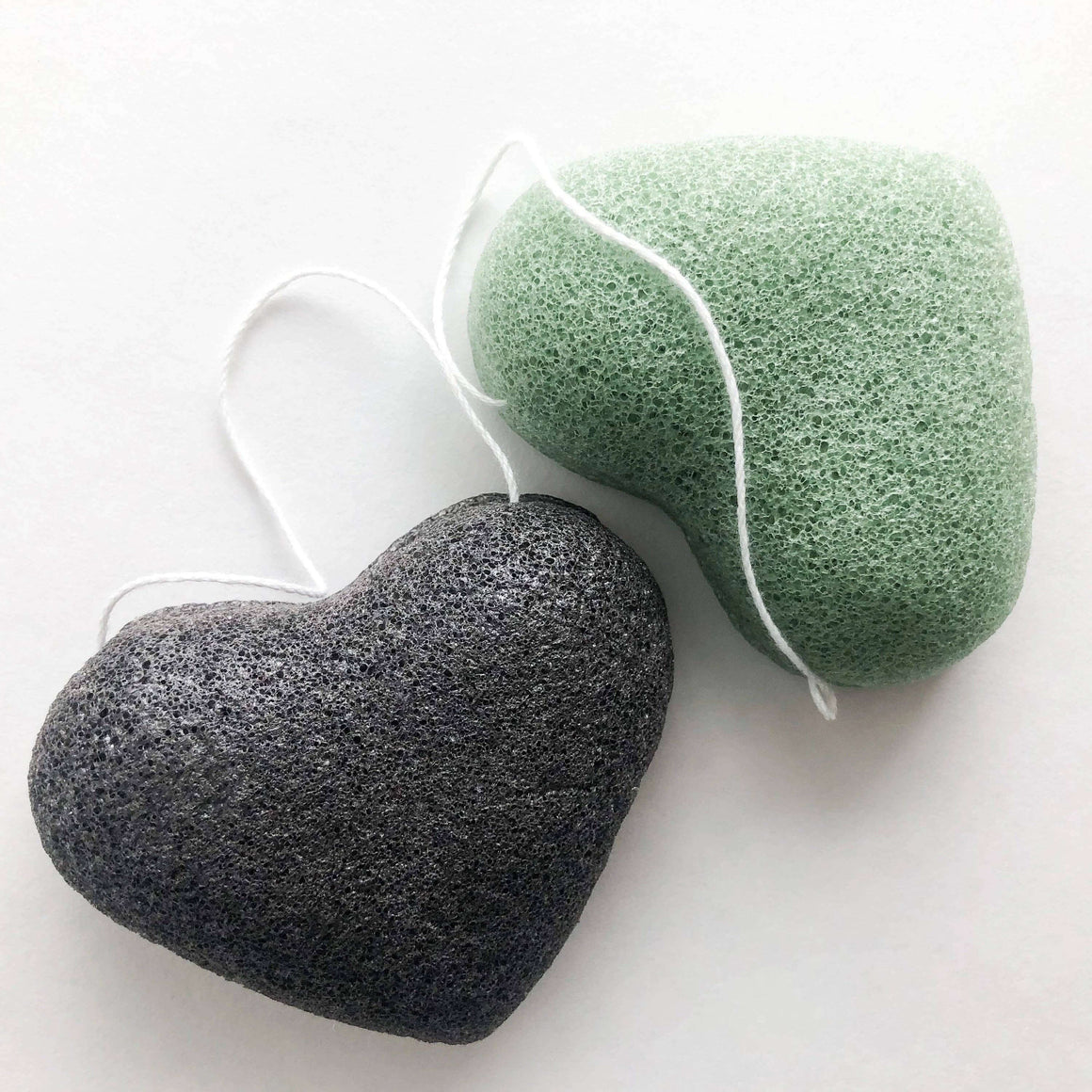 Two konjac sponges, one black and one green, on a white background.
