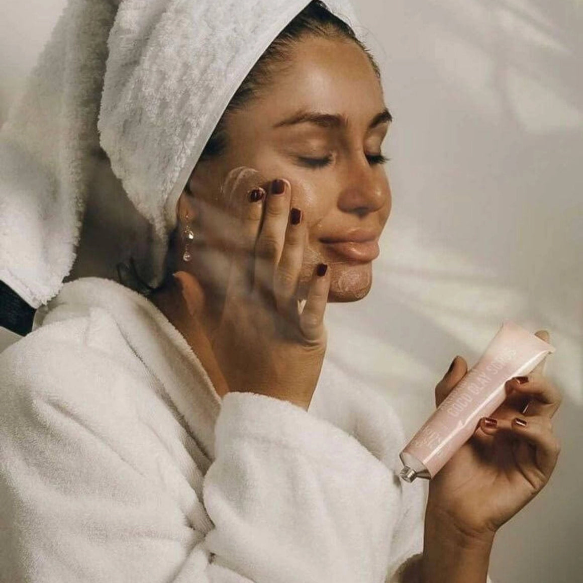 Woman applying skincare product with a towel on her head