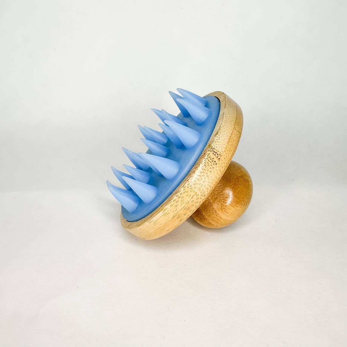 Blue spiked massager with wooden base on a light gray background