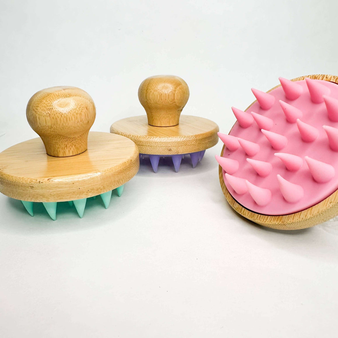 Two wooden brushes with green and purple bristles and a pink spiked brush on a white background.