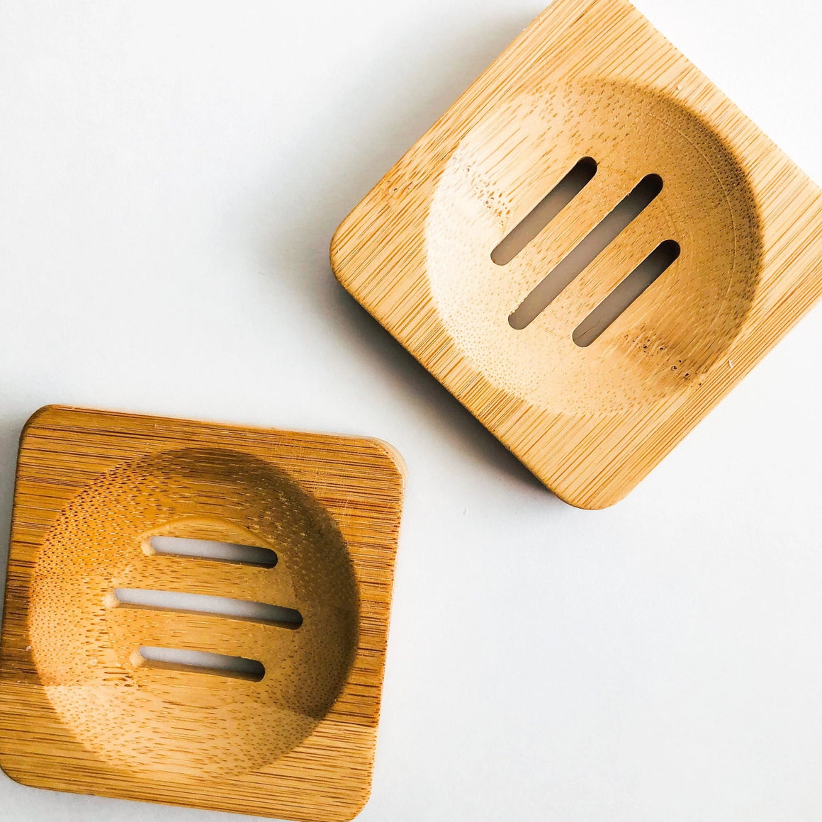 Two wooden soap dishes with slotted designs on a light background
