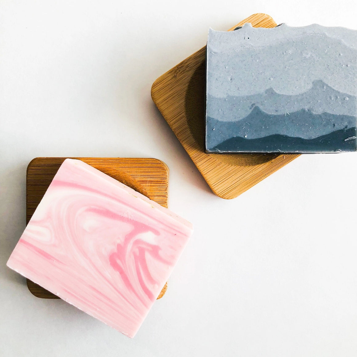 Two soap bars on wooden coasters with a white background