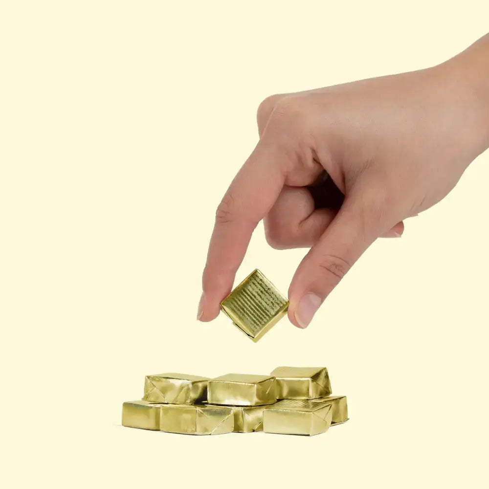 Hand holding a WonderBee® Chews piece above a stack of golden wrapped chews.
