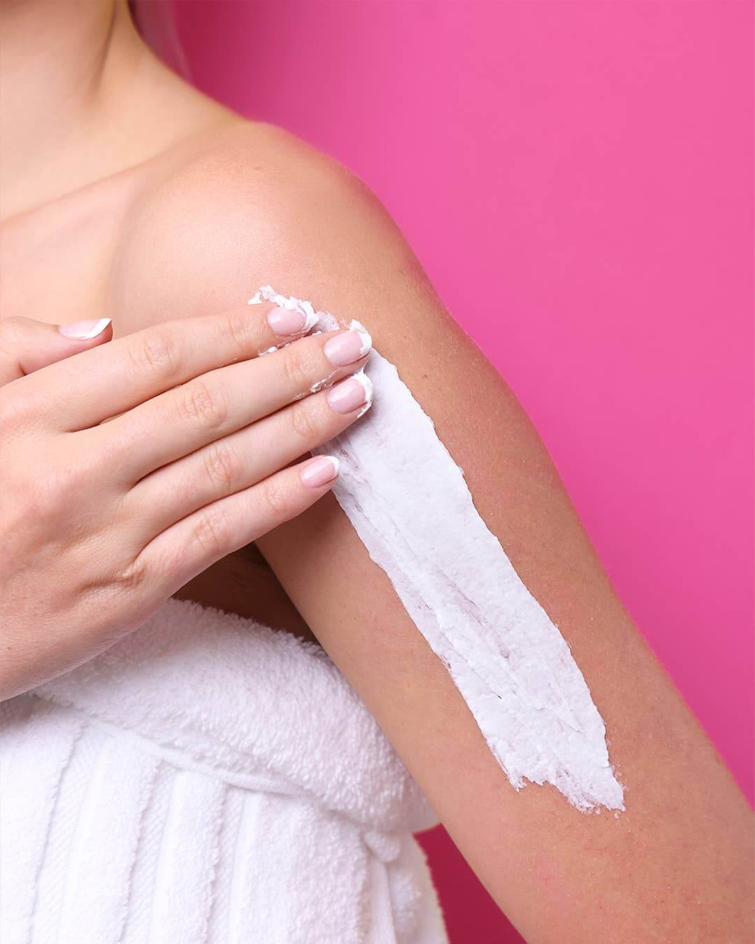 Person applying cream to their arm against a pink background