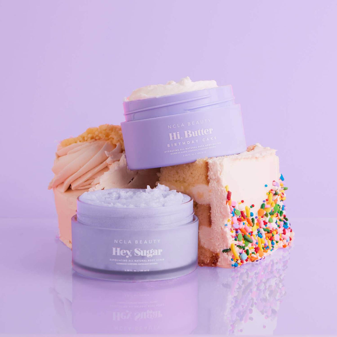 Two jars of NCLA Beauty cream on a purple background with cake slices.
