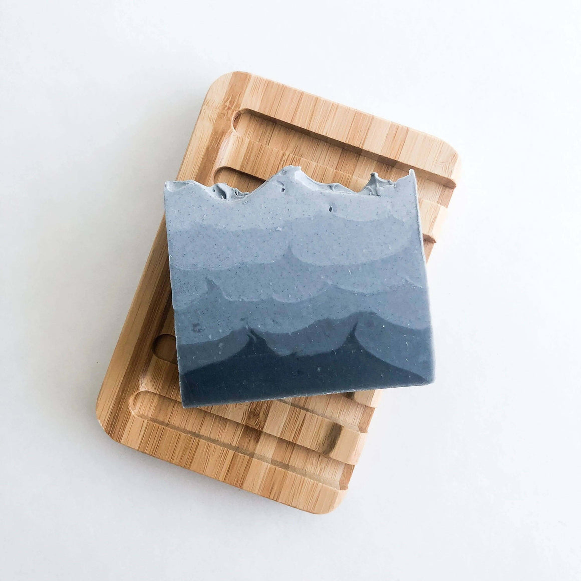 Blue soap bar with wavy texture on a wooden cutting board against a white background