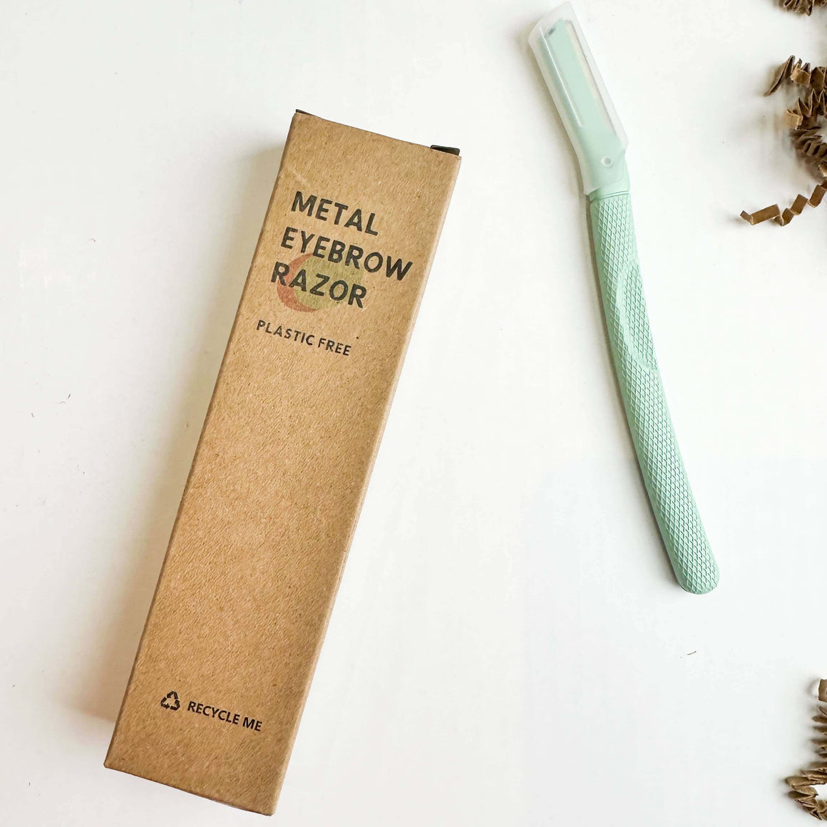 Metal eyebrow razor with cardboard packaging on a white background