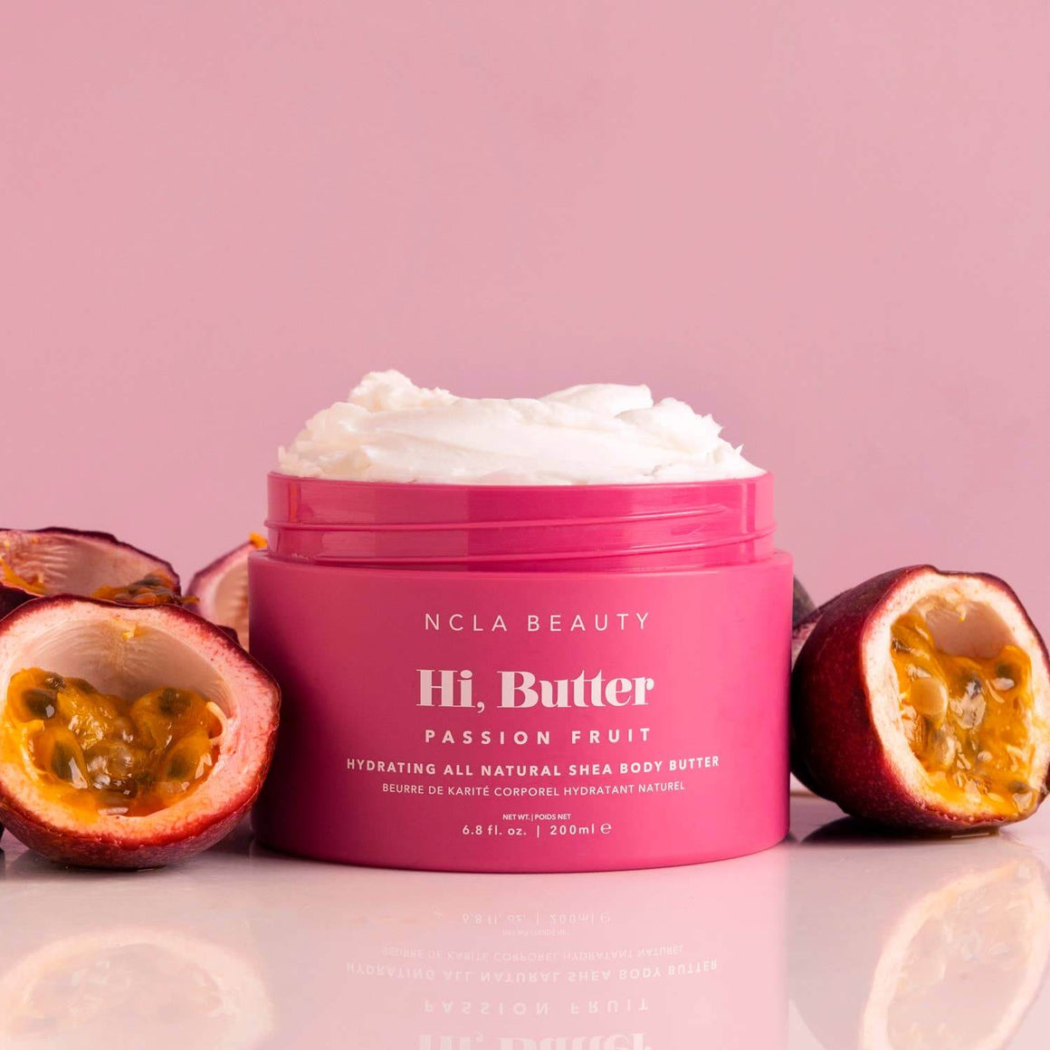 Pink jar of NCLA Beauty Hi, Butter Passion Fruit body butter with passion fruit halves on a pink background