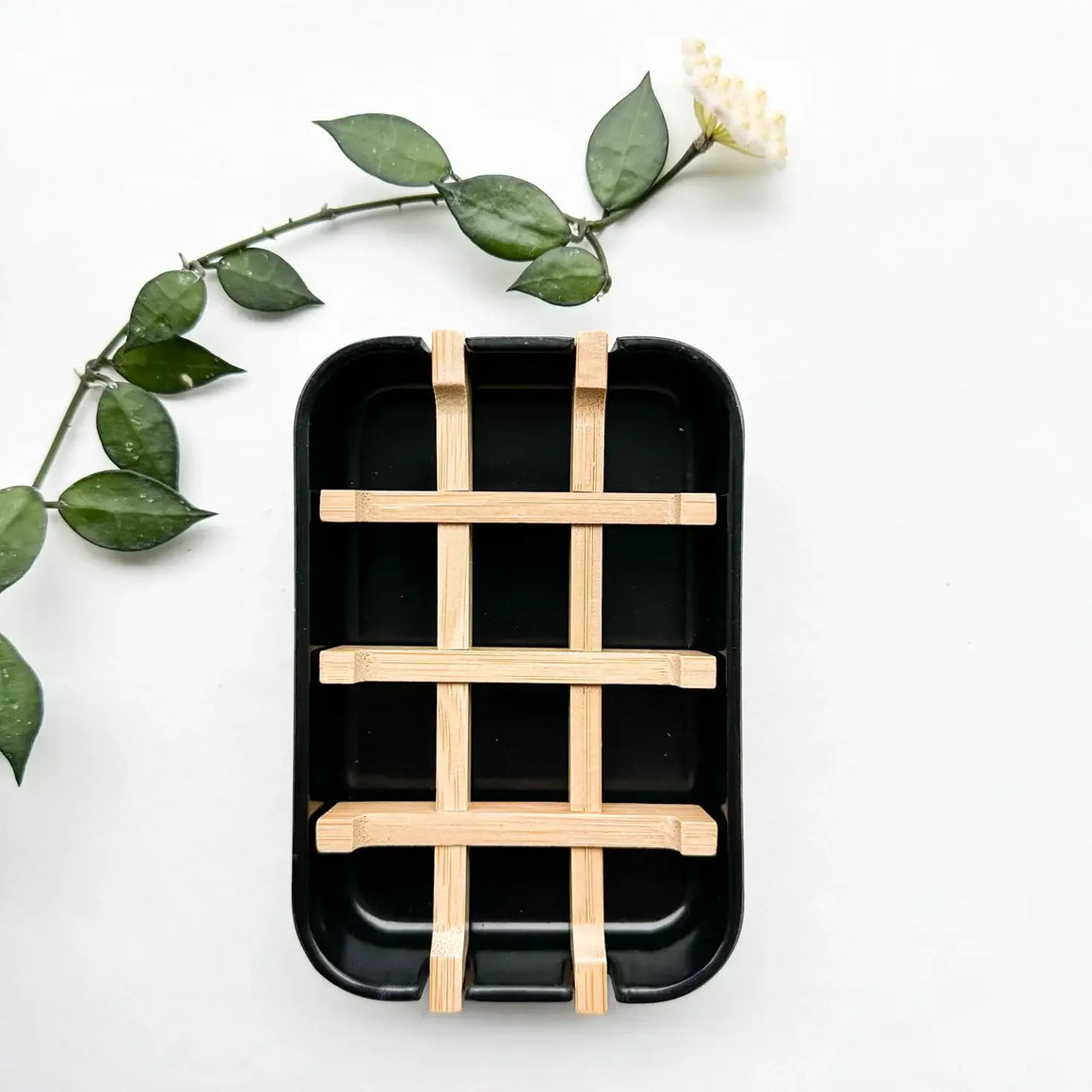 Black rectangular tray with wooden grid on a white background with green leaves.