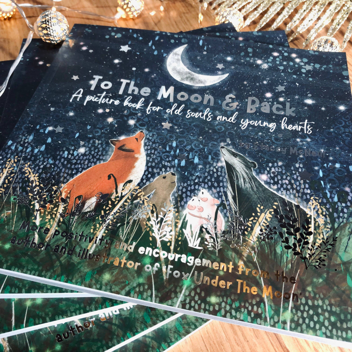 Children's book titled 'To The Moon & Back' with fox and wolf illustration on a wooden surface.