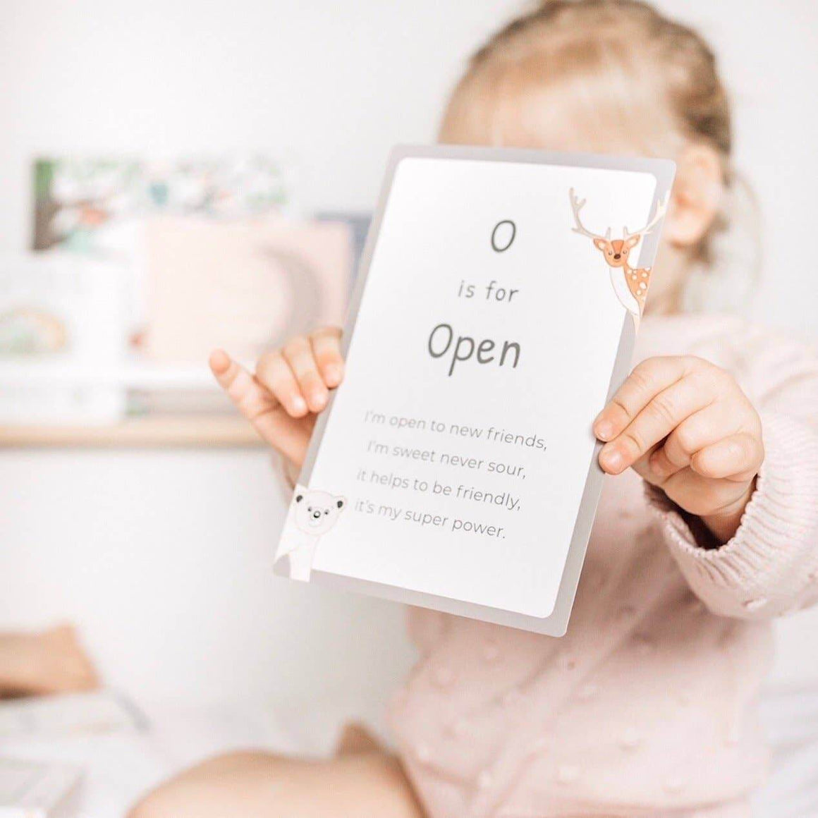 Child holding a book with text and a letter 'O' on a blurred background