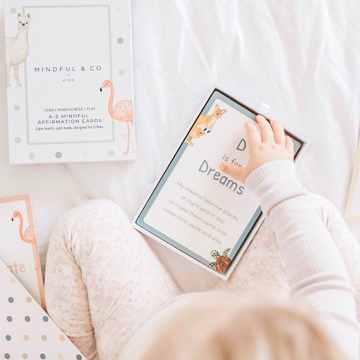 Child's hand holding a card with 'D is for Dreams' text, surrounded by other cards on a light surface.