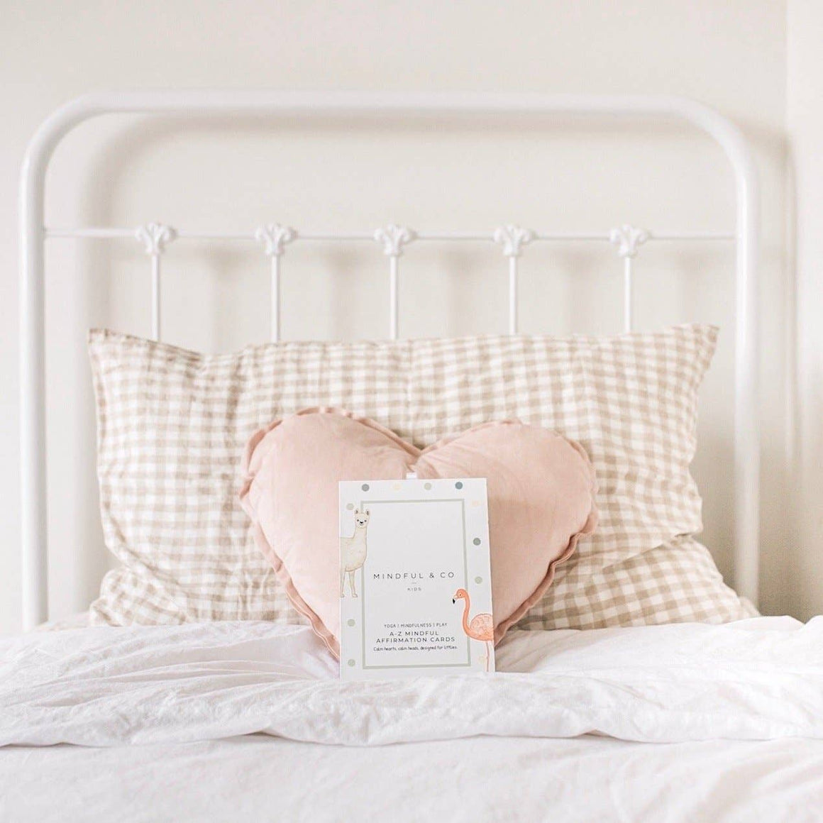Heart-shaped pink pillow on a bed with checkered pillows and a framed card in the center.