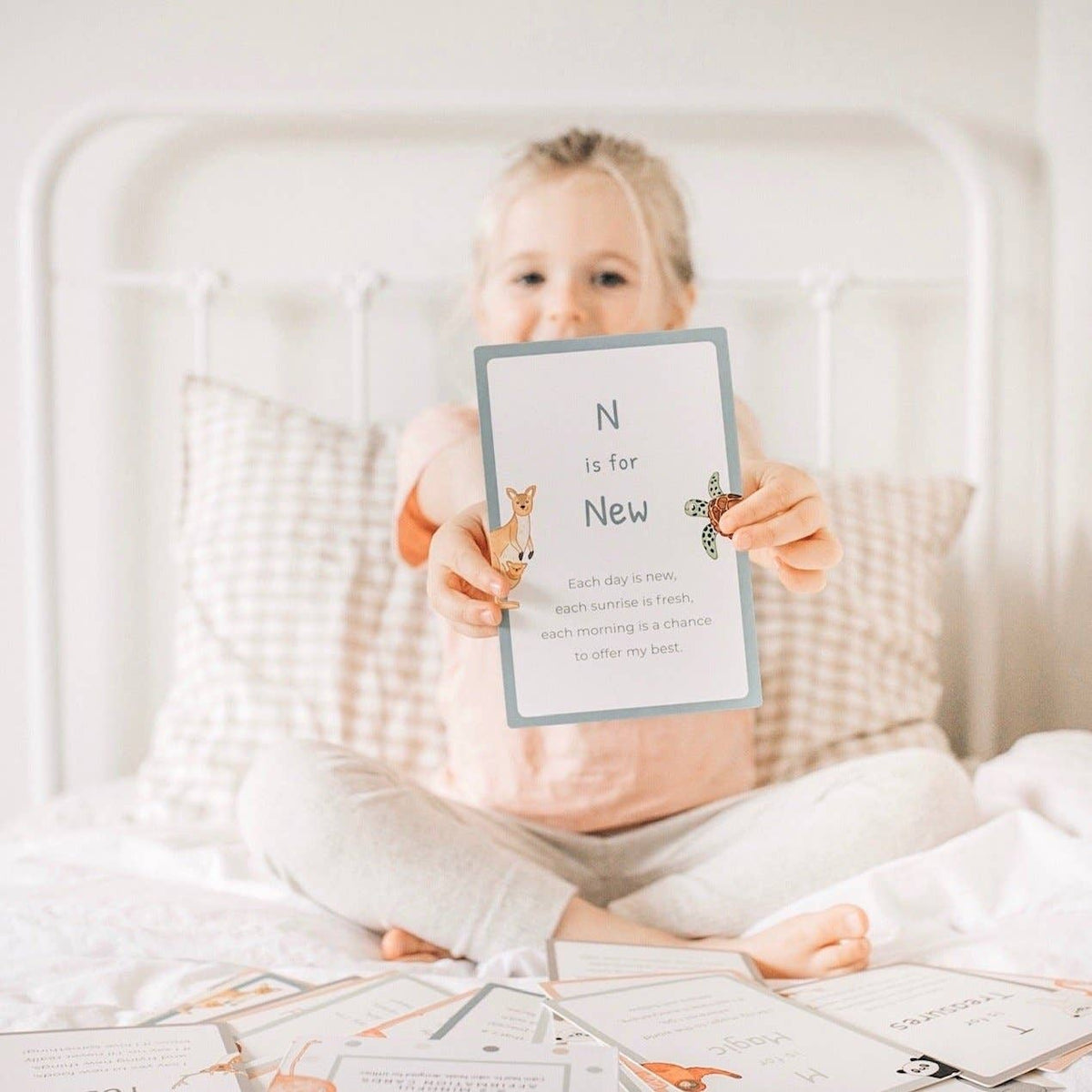 Child holding a card with 'N is for New' text on a bed