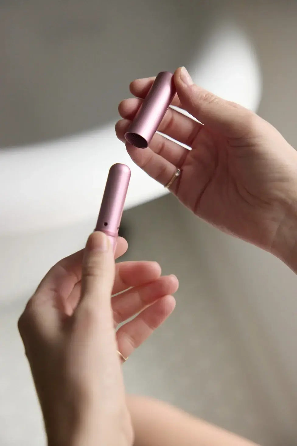 Two hands holding pink cylindrical objects against a neutral background