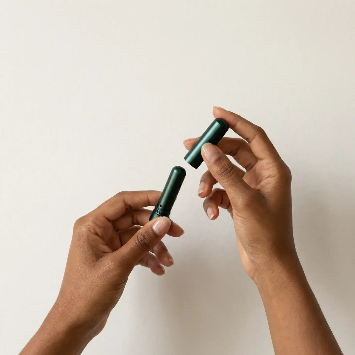 Two hands holding a green cylindrical object against a light background