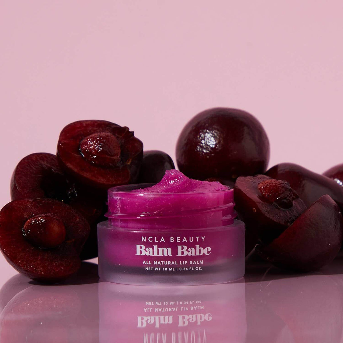 Purple lip balm jar labeled 'Balm Babe' with cherries on a pink background