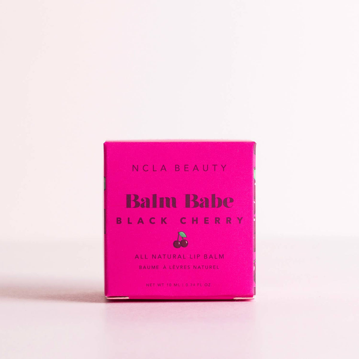 NCLA Beauty Balm Babe Black Cherry lip balm packaging on a pink background