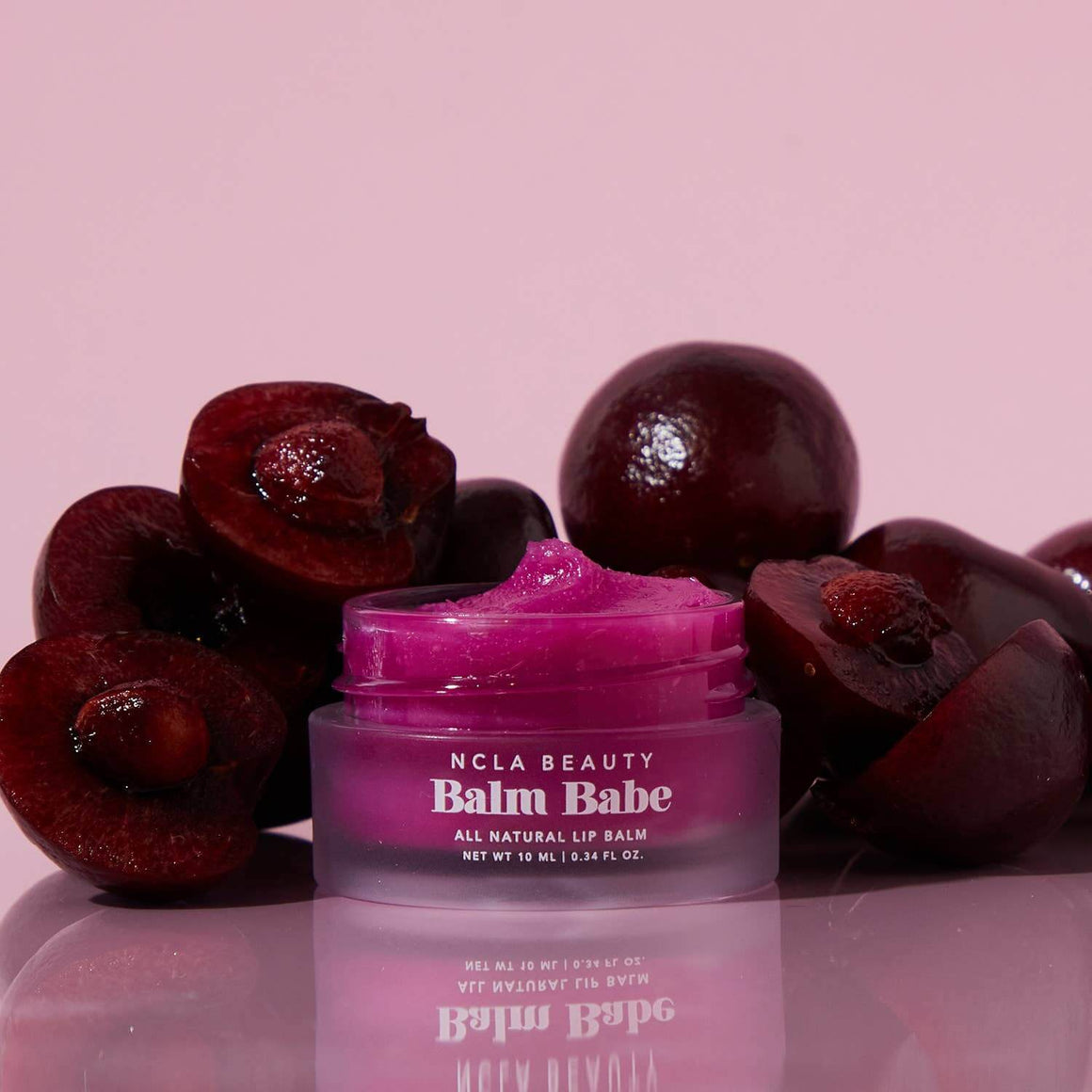 Purple lip balm jar labeled 'Balm Babe' with cherries on a pink background
