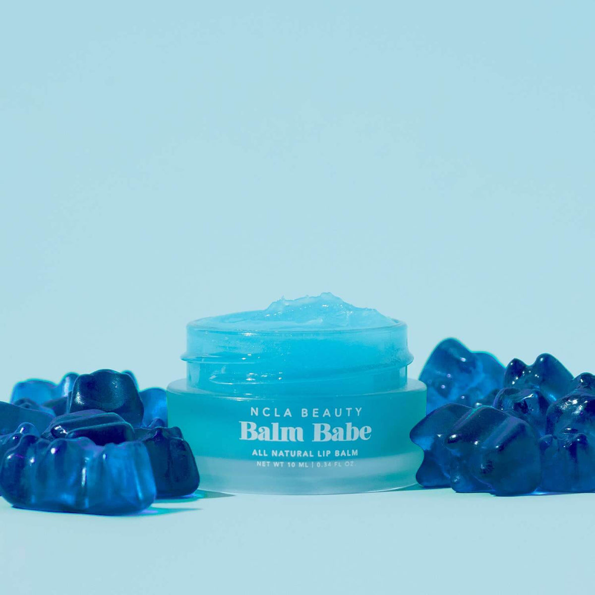 Blue lip balm container labeled 'Balm Babe' by NCLA Beauty on a light blue background