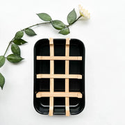 Black rectangular tray with wooden grid on a white background with green leaves.