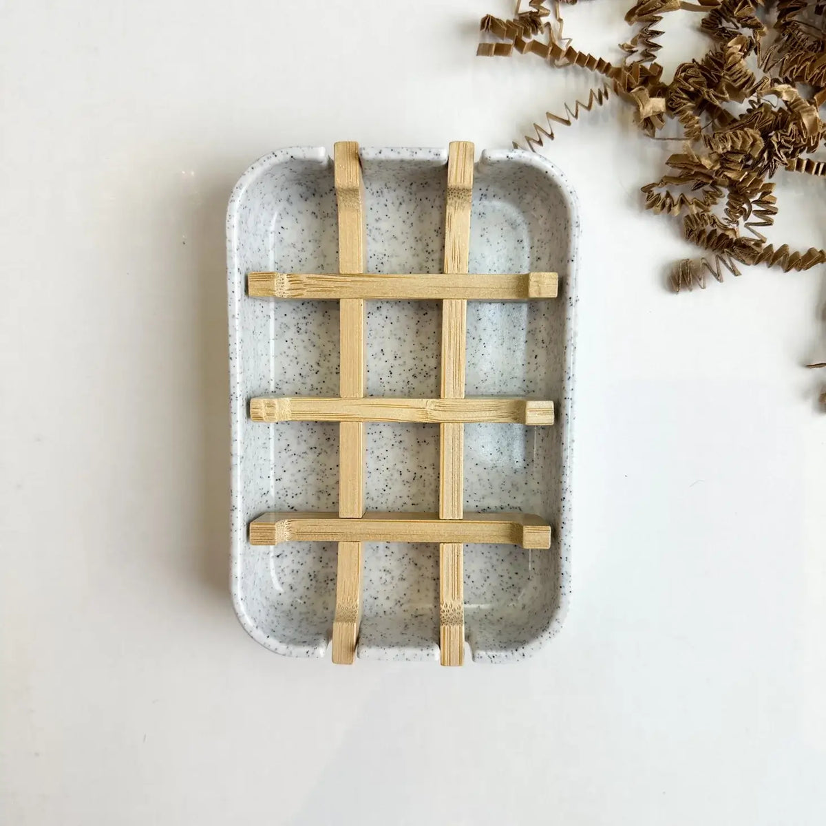 Speckled ceramic tray with woven wooden handle on a light background