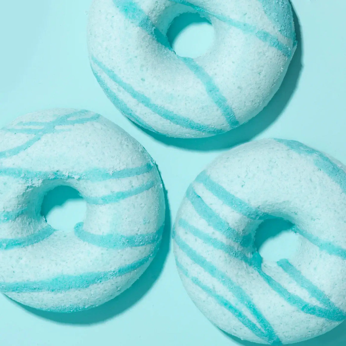 Three blue and white striped donut-shaped bath bombs on a light blue background