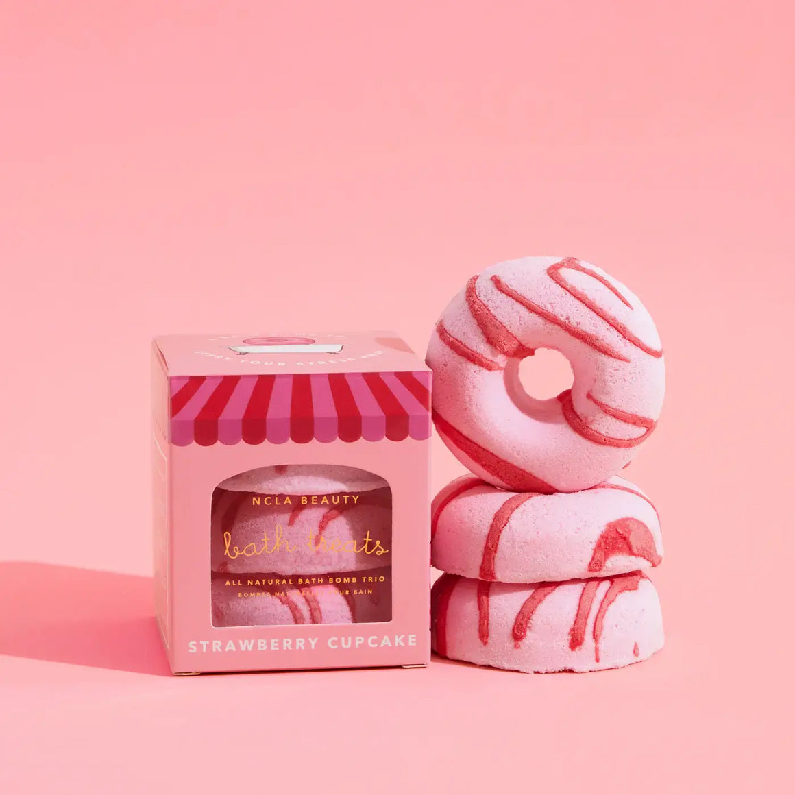 Pink bath bomb trio with a striped box on a pink background