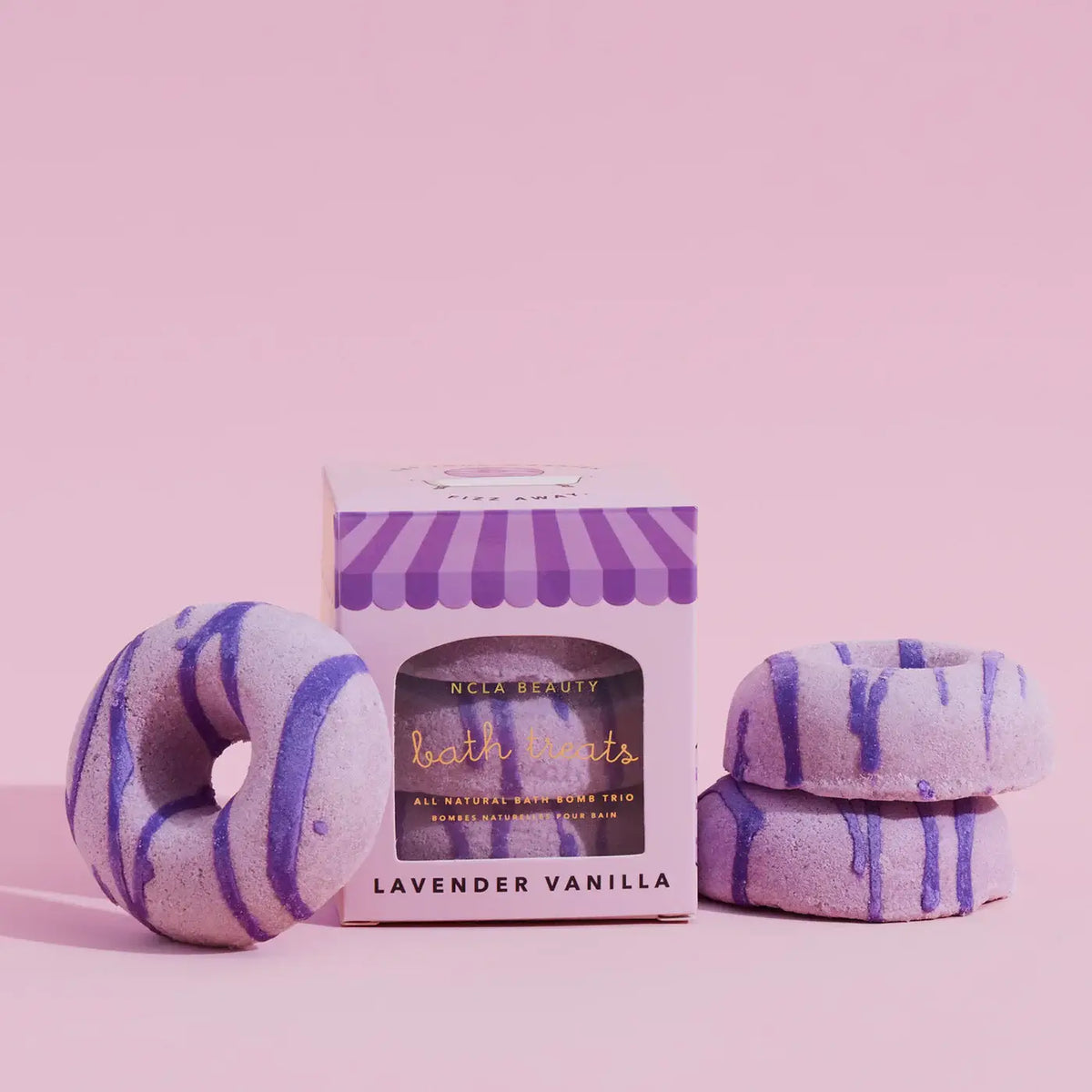 Bath bombs with purple stripes and a box labeled 'NCLA Beauty' on a pink background