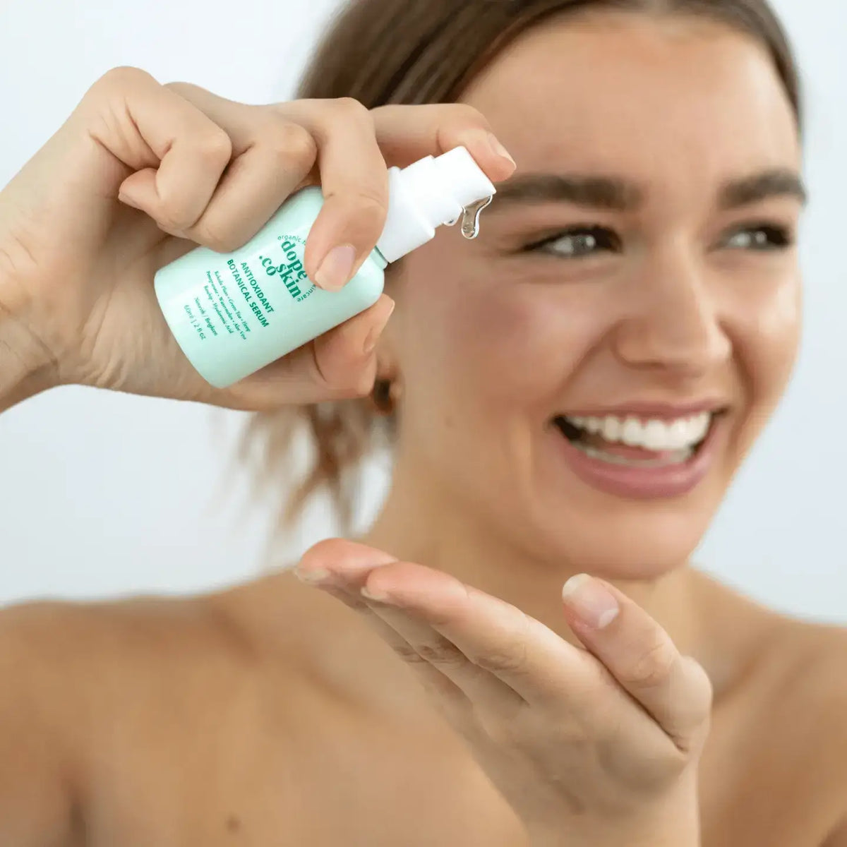 Woman applying a skincare product to her face with a close-up of the bottle.