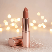 Lipstick with rose gold casing on a glittery surface with blurred lights in the background