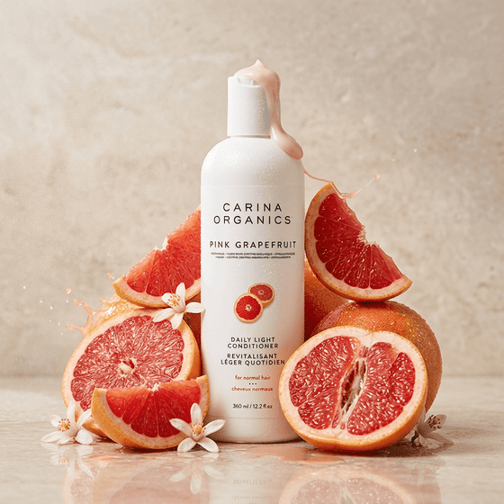 Carina Organics Pink Grapefruit skincare bottle surrounded by pink grapefruit slices on a neutral background