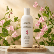 Carina Organics Sweet Pea skincare product on a wooden board with flowers in the background