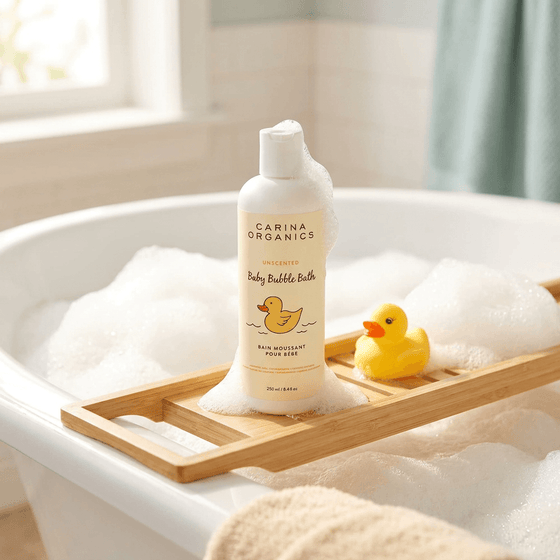Carina Organics baby bubble bath bottle on a wooden tray with a rubber duck in a bathtub filled with bubbles.