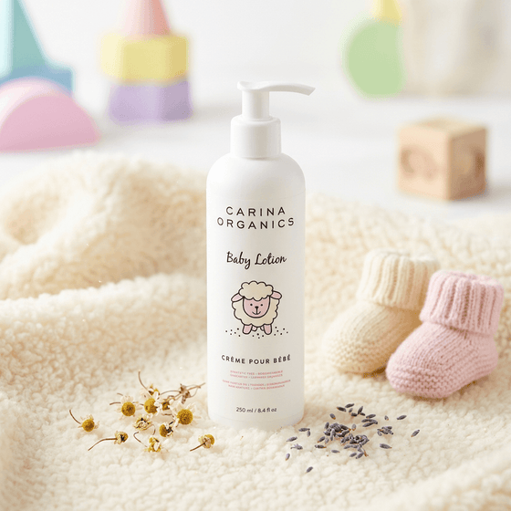 Carina Organics baby lotion bottle on a soft surface with baby boots and flowers.
