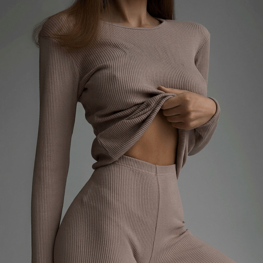 Person wearing a beige ribbed sweater and pants against a gray background