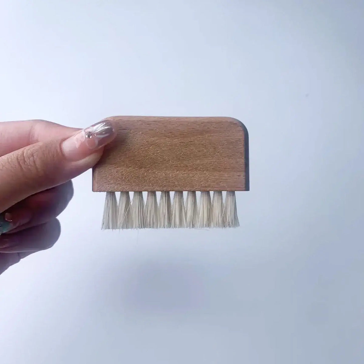 Small wooden brush with bristles held by a hand against a light blue background