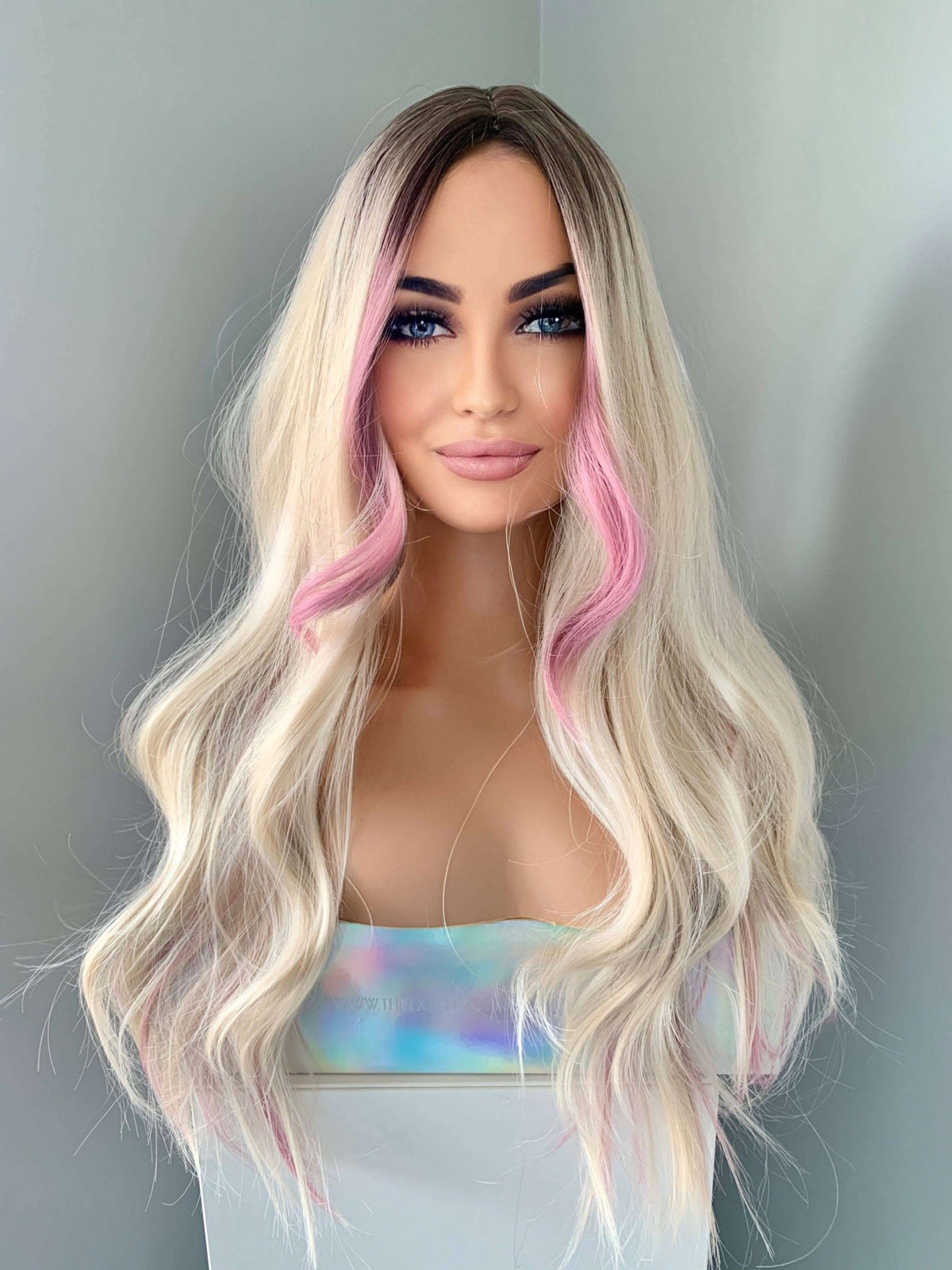 Mannequin head with long blonde wig with pink ends on a plain background