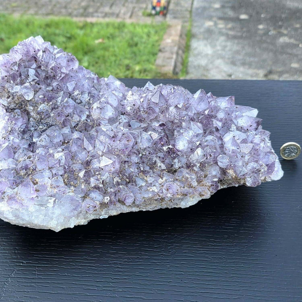 Amethyst crystal cluster on a dark surface with a ruler for scale.