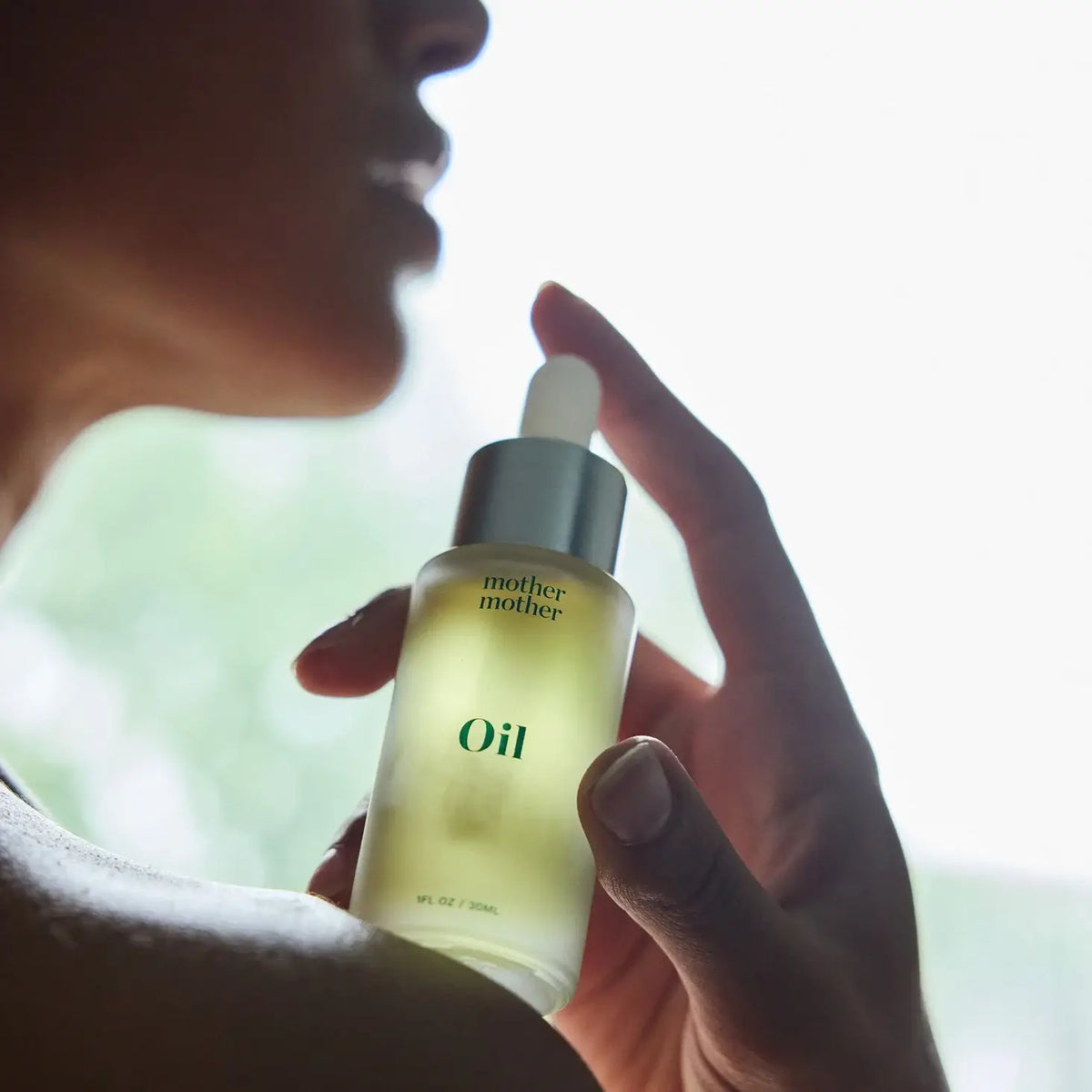 Hand holding a bottle of 'mother' oil with a blurred background
