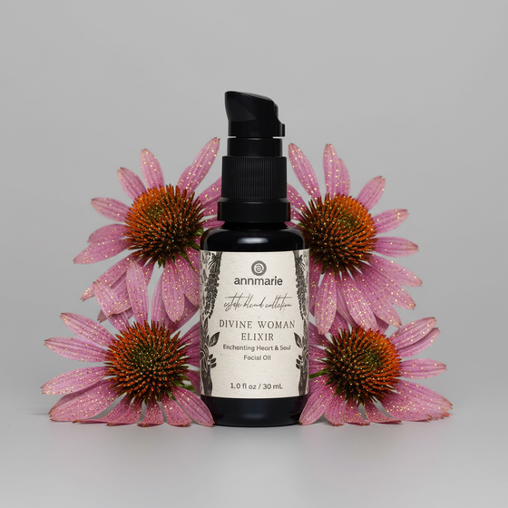 Black bottle labeled 'Divine Woman Elixir' surrounded by pink flowers on a gray background