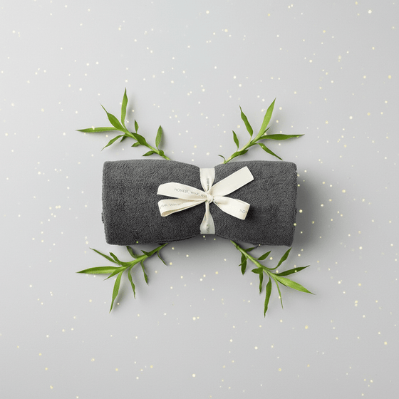 Gray folded fabric with a white ribbon and green leaves on a light gray background